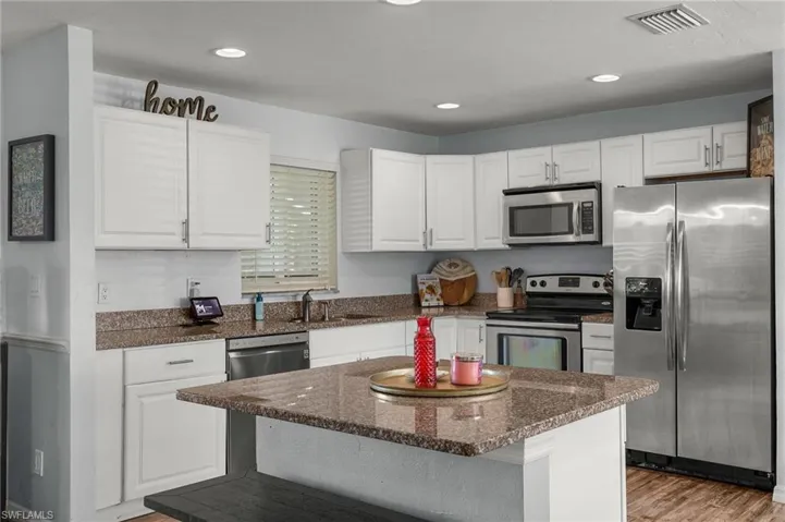 Kitchen with sink, white cabinetry, a center island, appliances with stainless steel finishes, and light hardwood / wood-style floors