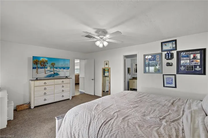 Bedroom with ceiling fan, connected bathroom, and dark carpet