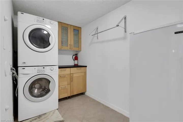Laundry area featuring a textured ceiling, cabinet space, light tile patterned floors, and stacked washing machine and dryer