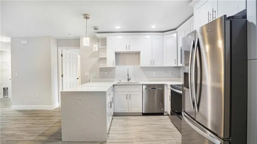 Kitchen with stainless steel appliances, sink, white cabinets, light hardwood/wood-style floors, and hanging light fixtures