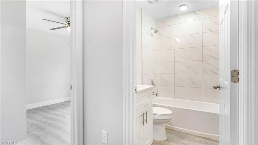 Full bathroom featuring vanity, tiled shower / bath combo, ceiling fan, hardwood/wood-style flooring, and toilet