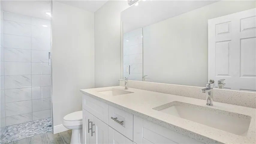 Bathroom featuring a tile shower, dual vanity, wood-type flooring, and toilet