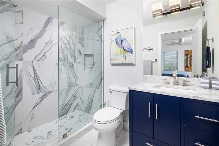 Bathroom with a tile shower, vanity, toilet, and ceiling fan