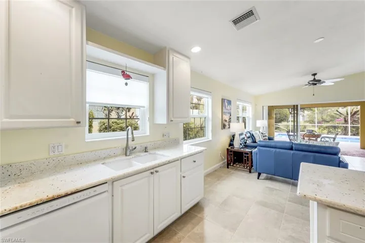 Kitchen sink area with light-toned countertops, white cabinetry, and a window overlooking exterior greenery