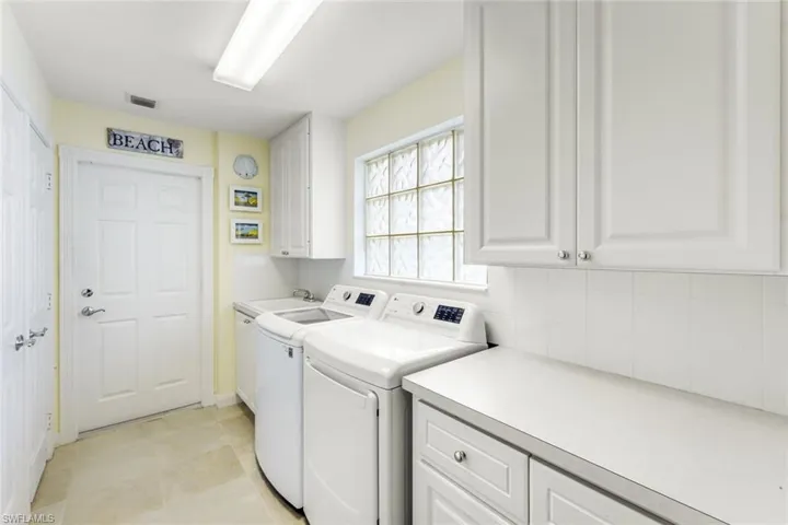 Dedicated utility space featuring ample white cabinetry, a glass block window, light-toned flooring, and a countertop with storage below