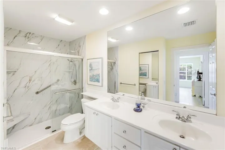 Bathroom featuring a dual vanity with white cabinetry, a spacious mirror, and a shower with sliding glass doors