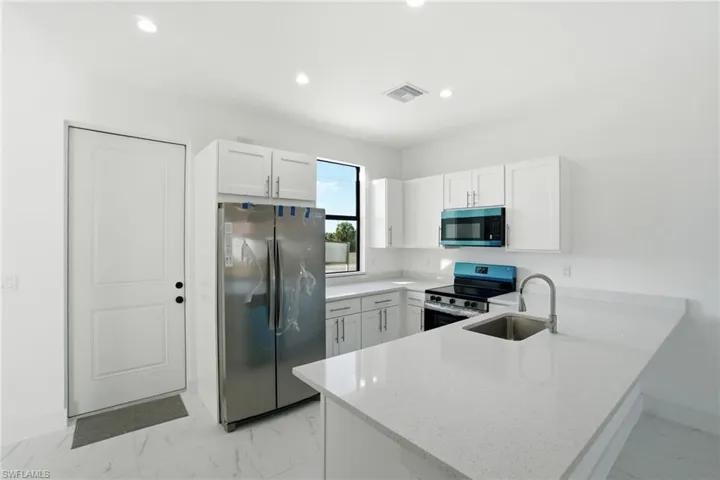 Kitchen featuring stainless steel appliances, a peninsula, white cabinets, light stone counters, and light marble finish floors