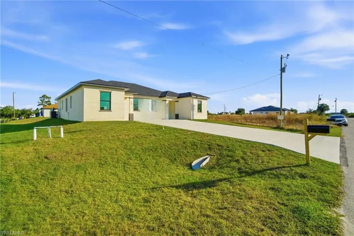 View of front facade featuring driveway, stucco siding, and a front lawn