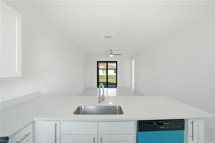 Kitchen featuring dishwashing machine, open floor plan, white cabinets, a peninsula, and light stone counters