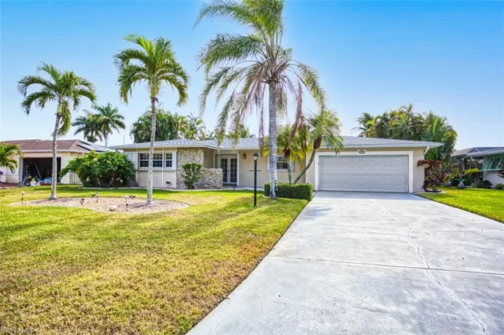 Ranch-style home featuring driveway, a front lawn, an attached garage, french doors, and stucco siding
