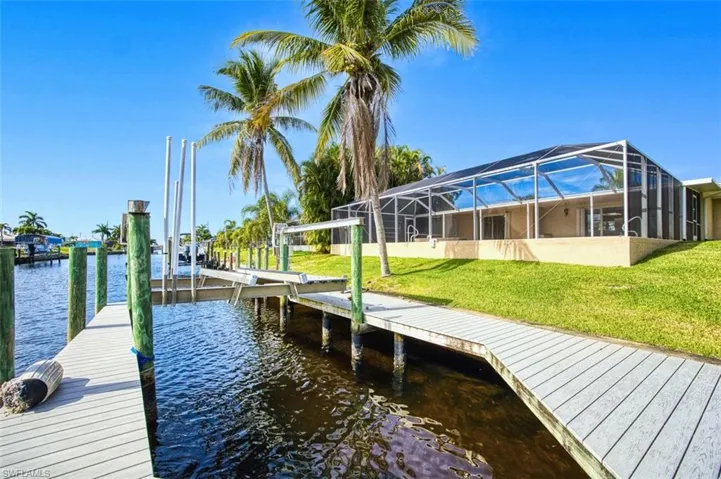Dock area featuring a sunroom, a lanai, a lawn, a water view, and boat lift. Added feature of a kayak lift.