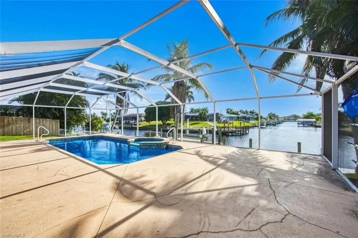 View of pool featuring glass enclosure, a pool with connected hot tub, a water view, and a sunroom