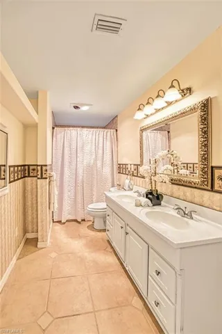 Full bath with curtained shower, double vanity, and a wainscoted wall
