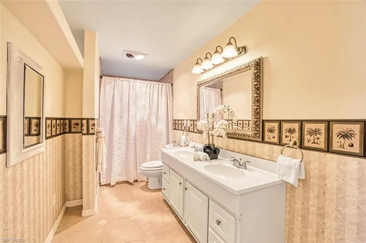 Primary bathroom featuring wainscoting, double vanity, a shower with curtain, and light tile patterned flooring