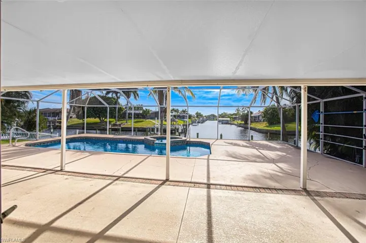 View of pool featuring a sunroom, a patio area, a water view, and glass enclosure