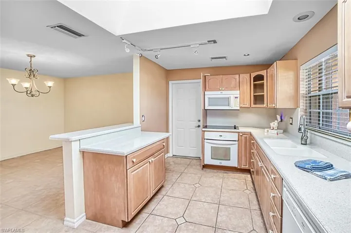 Kitchen with glass insert cabinets, white appliances, track lighting, decorative light fixtures, and light brown cabinetry