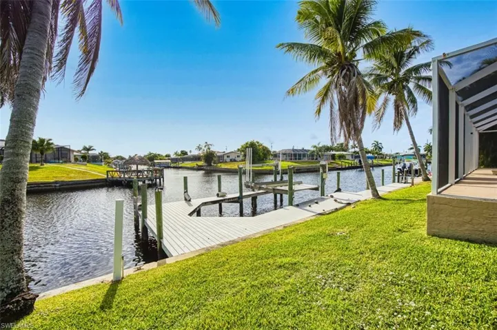 Dock area with boat lift, a water view, a lawn, and a residential view