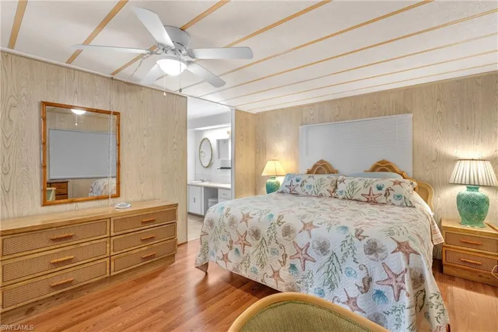 Bedroom with wooden walls, wood finished floors, ensuite bath, and ceiling fan