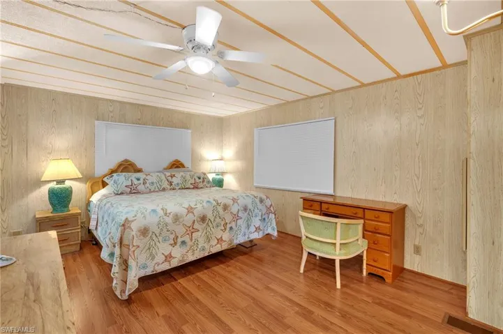 Bedroom with wood finished floors, ceiling fan, and wood walls