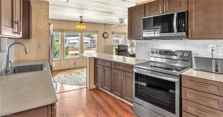 Kitchen featuring stainless steel appliances, a peninsula, light wood-type flooring, light countertops, and decorative light fixtures