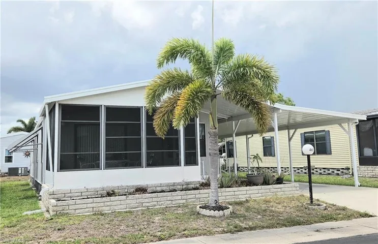 White exterior with a covered carport, screened-in porch, mature palm tree, and a stone-look planter box