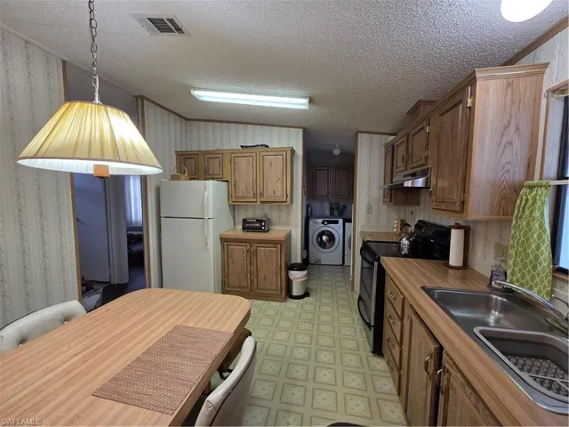 Kitchen featuring wood-finish laminate countertops, natural wood cabinetry, double stainless steel sink, and smooth-top stove.