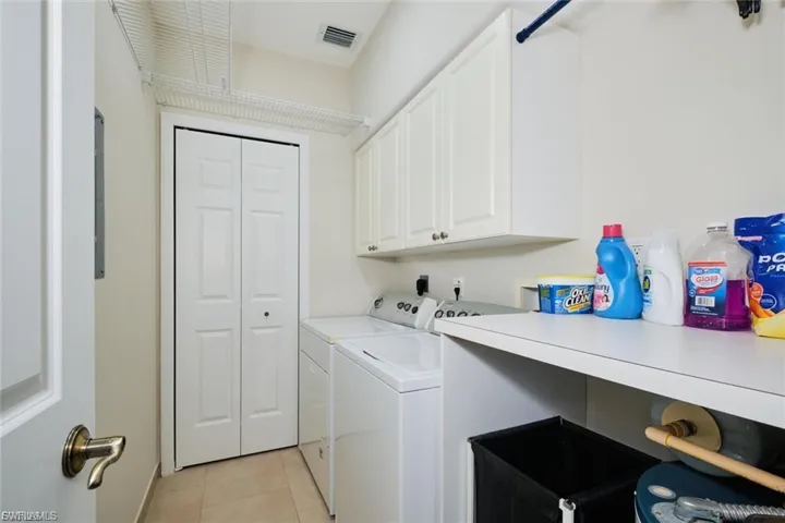 Dedicated laundry area featuring a washer and dryer, upper cabinetry, a utility shelf, and tile flooring