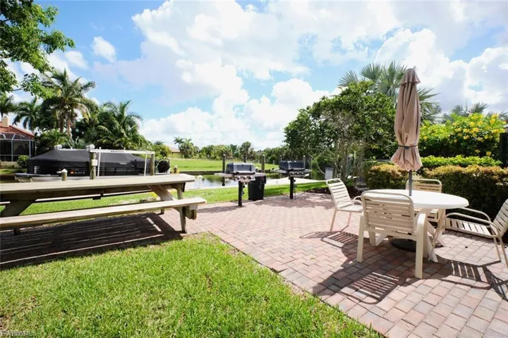 Brick paver patio with a picnic table and additional outdoor seating, bordered by a green lawn and mature landscaping