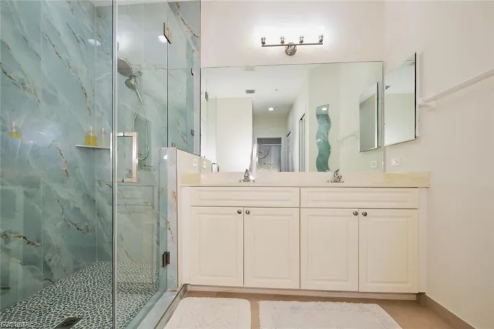 Glass-enclosed shower with blue-toned marbled walls and a mosaic pebble floor