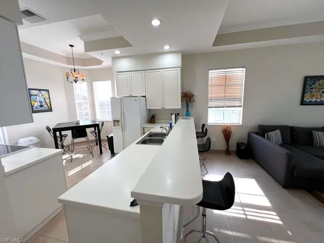 Open-concept living space featuring a kitchen island with seating, recessed lighting, white cabinetry, and tray ceilings