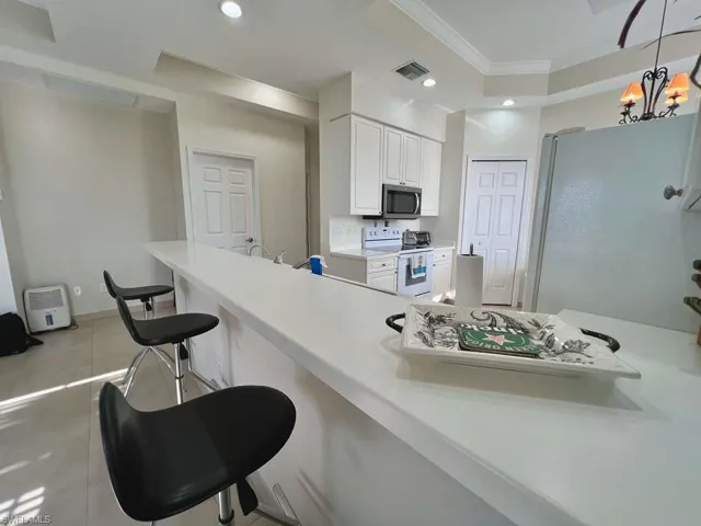 Spacious kitchen featuring a long breakfast bar with a solid surface countertop, white cabinetry, integrated stainless steel microwave, and white range