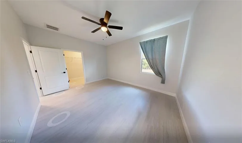 Unfurnished bedroom with a walk in closet, light wood-style floors, and a ceiling fan