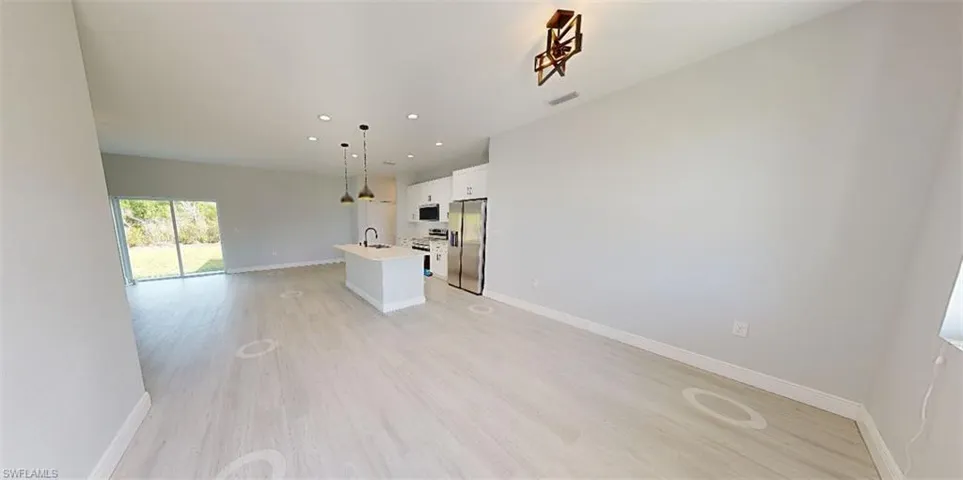Kitchen featuring open floor plan, white cabinetry, an island with sink, stainless steel appliances, and light wood-style floors