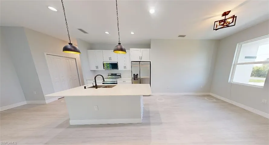 Kitchen with white cabinets, an island with sink, decorative light fixtures, stainless steel appliances, and light wood-style flooring