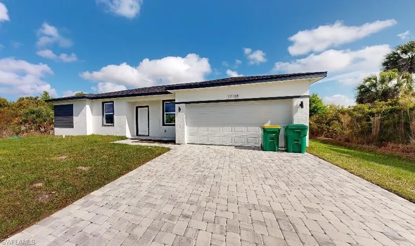 Single story home with a front yard, stucco siding, decorative driveway, and an attached garage