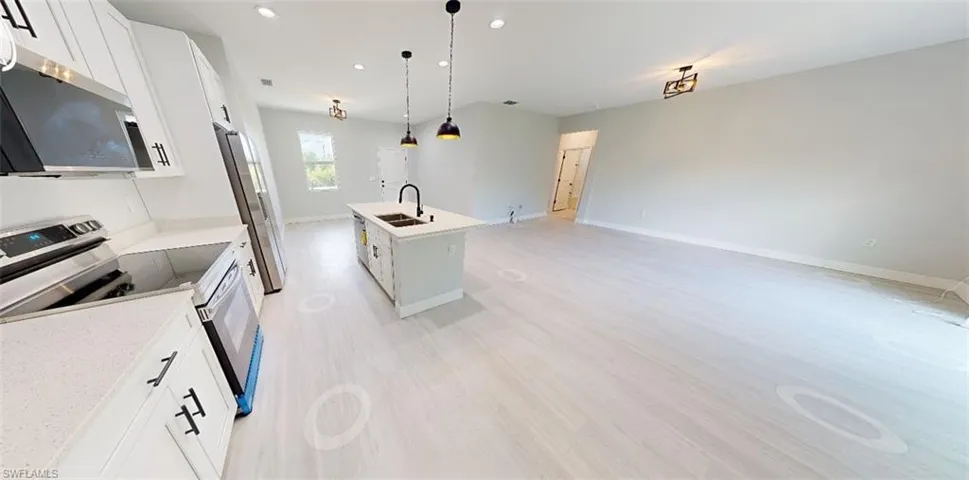 Kitchen with white cabinetry, stainless steel appliances, a kitchen island with sink, open floor plan, and decorative light fixtures