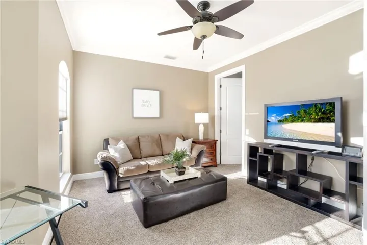 Living area with ornamental molding, light colored carpet, and a ceiling fan