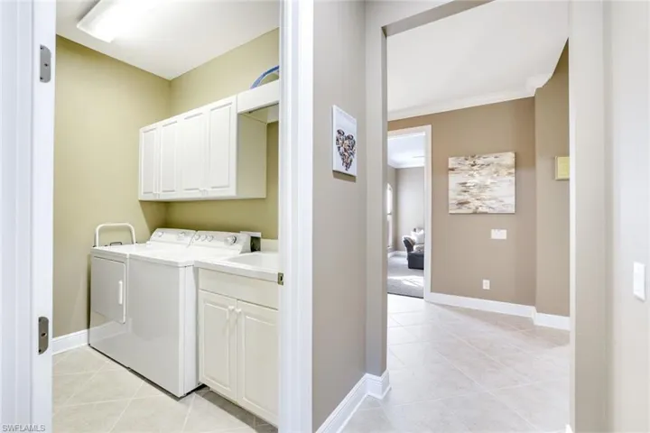Laundry room featuring light tile patterned floors, cabinet space, washer and clothes dryer, and crown molding