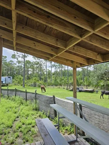 Exposed wood beam ceiling structure with a wood-planked overhead, overlooking a fenced grassy expanse