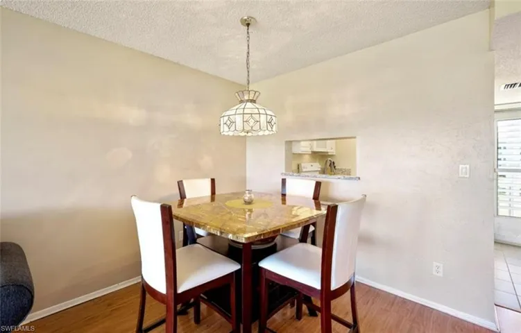 Dining area featuring wood-look flooring, a pass-through window to the kitchen, and a decorative overhead light fixture