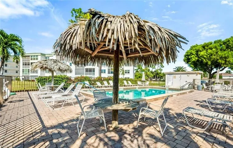 The property features a swimming pool surrounded by a paved patio with lounge chairs and a tiki umbrella