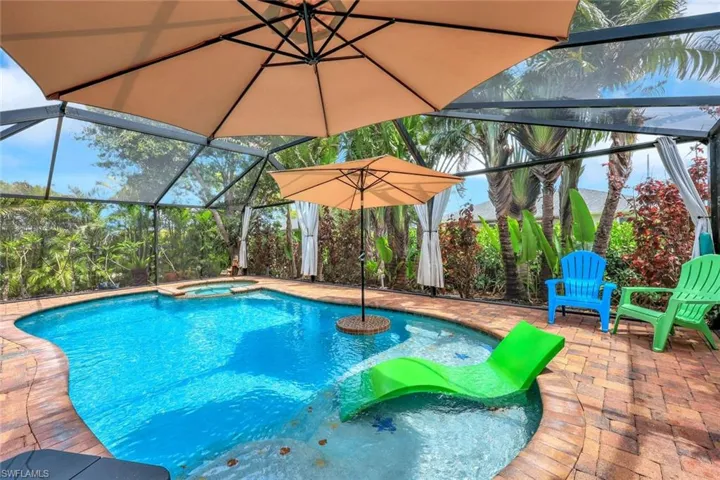 View of swimming pool featuring a patio, a pool with connected hot tub, and glass enclosure