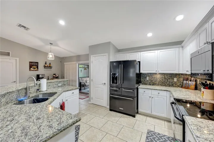 Kitchen with black fridge, a sink, stainless steel microwave, decorative backsplash, and white cabinetry