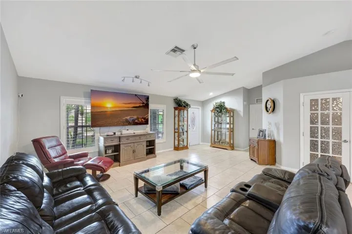 Living room with vaulted ceiling, light tile patterned flooring, ceiling fan, and baseboards