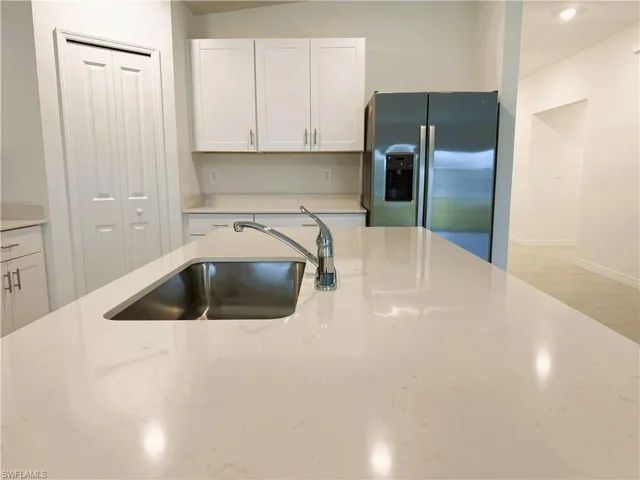 Kitchen with stainless steel fridge, white cabinetry, and light stone countertops