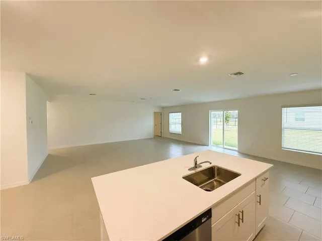 Kitchen with open floor plan, a kitchen island with sink, white cabinetry, and light stone countertops