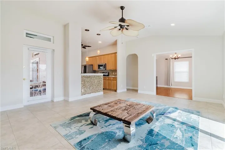 Living area featuring arched walkways, ceiling fan with notable chandelier, light tile patterned floors, and high vaulted ceiling