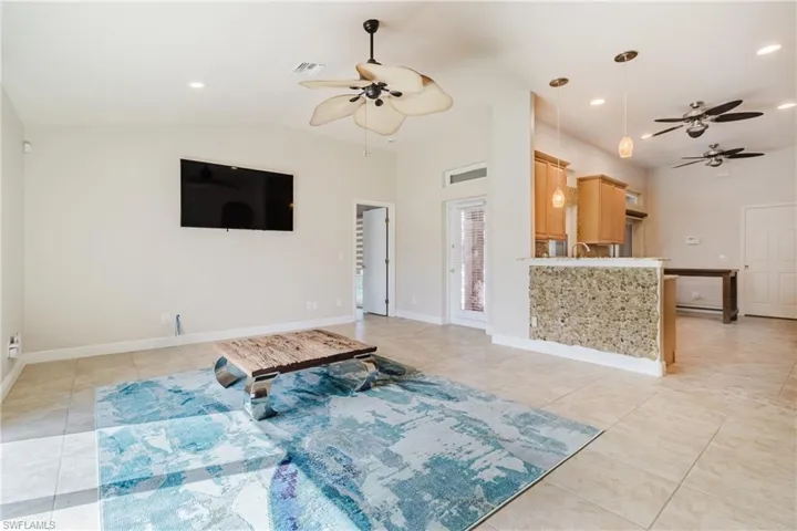 Living area with lofted ceiling, visible vents, light tile patterned floors, and ceiling fan