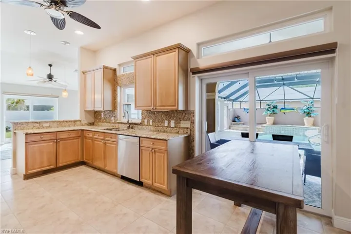 Kitchen with light stone counters, a ceiling fan, backsplash, stainless steel dishwasher, and a sink