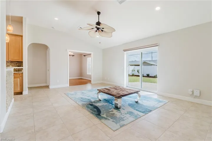 Living room featuring light tile patterned flooring, arched walkways, ceiling fan, and vaulted ceiling